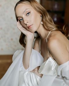 a woman in a white dress sitting on a couch with her hand under her chin