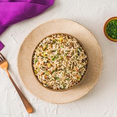 a bowl filled with rice and vegetables next to a fork on a white tablecloth