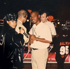 a group of people standing around each other in front of a microphone and some onlookers