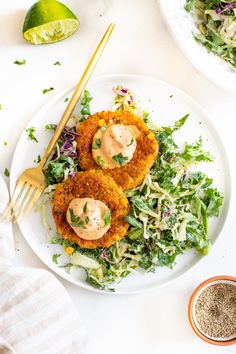 two fish cakes on a white plate with coleslaw and dressing next to it