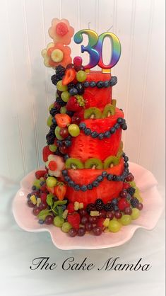 a three tiered cake decorated with fruit and the number 30 on top is displayed