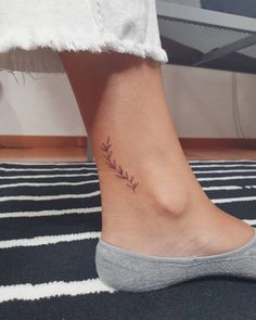 a woman's foot with a small branch tattoo on the side of her ankle