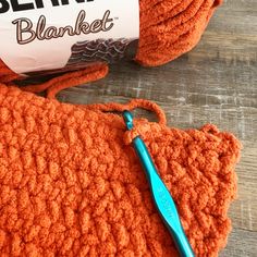 an orange crochet bag with a blue knitting needle on it and a ball of yarn in the background