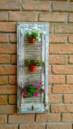 an old window is decorated with potted plants and hanging on the brick wall behind it