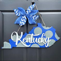 a kentucky state shaped door hanger with the word kentucky painted on it and a blue polka dot bow