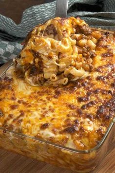 a casserole dish with pasta and meat in it on a wooden table next to a fork