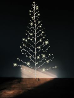 a small white christmas tree with lights on it's branches in front of a dark background