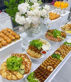 an assortment of appetizers and snacks displayed on a buffet table with flowers in the background