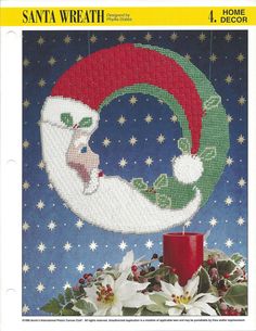 a cross stitch christmas card with a santa hat hanging from the top of a crescent