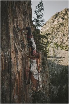 two people are climbing up the side of a mountain with their arms around each other