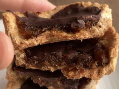 a person is holding up some chocolate covered cookie bars on a plate with their fingers