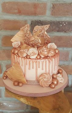 a cake decorated with gold and white icing on top of a wooden table next to a brick wall