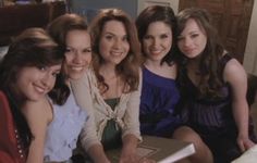 a group of women sitting next to each other in front of a table with an open book on it