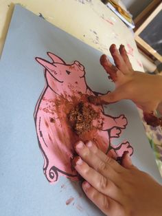 a child's hand is holding something in front of a drawing of a pig