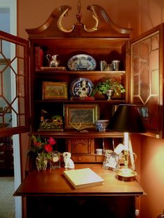 a wooden desk topped with lots of books and vases next to a lamp on top of a table