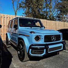 a blue mercedes g - class parked in a parking lot next to a wooden fence