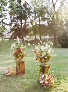 two tall vases with flowers are sitting in the grass