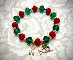 "✿ Beautiful Christmas bracelet in an easy-to-wear strong stretchy cord. Simply elegant! ♥ The bracelet is created using 10mm red and green crystal rondelles in a strong stretchy cord. The crystals are separated by smooth 14K plated gold hematite spacer beads. ♥ The multifaceted crystals catch light at your every move. Stunning! ♥ The intricately-cut initial charm (15mm) will add personalization to your bracelet. ♥ Meaningful \"Noel\" charm measures 15 x 20 mm ✿ This item comes in a dainty sheer Gold Beaded Bracelets For Christmas, Red Stretch Bracelet For Christmas, Red Stretch Bracelet For Christmas Holiday, Red Beaded Stretch Bracelet For Christmas, Green Crystal Bracelet, Christmas Bling, Braided Bracelet Diy, Holiday Beading, Red Bracelet