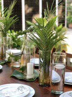 a wooden table topped with lots of plates and vases filled with plants next to candles