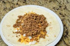 a tortilla topped with ground beef and cheese on top of a white plate