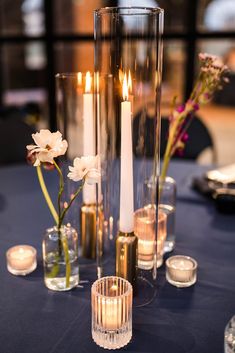 candles and vases on a table with flowers in the center, surrounded by glass containers