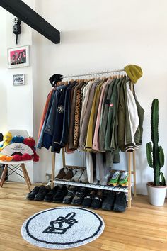 a rack with clothes and shoes on it in a room next to a potted cactus