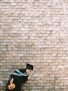 a woman in a graduation gown leaning against a brick wall