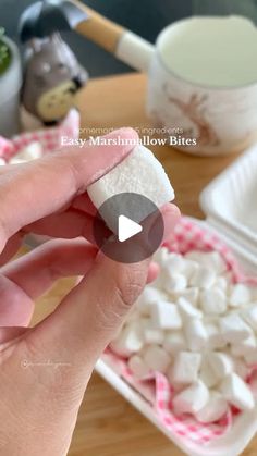 someone holding marshmallows in their hand on a wooden table with other food items