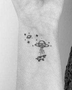 a small tattoo on the wrist of a woman with an alien and dog flying through the sky