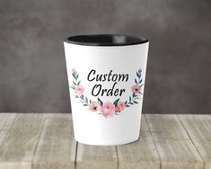 a white and black coffee cup with the words custom order printed on it sitting on a wooden table