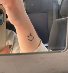 a woman's arm with a smiley face tattoo on her left wrist, in front of a mirror