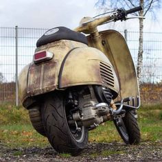 an old, rusted motorcycle is parked in the grass near a fenced area