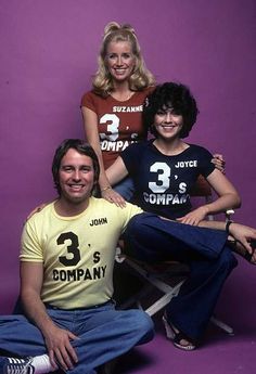 three women and one man are posing for a photo in front of a purple background