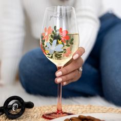 a woman is holding a wine glass with flowers on it