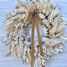 a wreath made out of dried flowers and leaves on a white wooden background with a brown ribbon