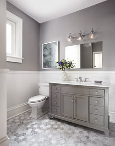 a white toilet sitting next to a gray sink in a bathroom under two mirrors and lights