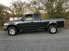 a green pick up truck is parked on the side of the road in front of some trees