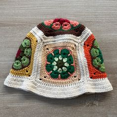 a crocheted hat with flowers and leaves on the front, sitting on a wooden surface