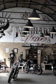 several motorcycles are parked in a garage with lights hanging from the ceiling and signs on the wall