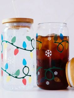 two mason jars filled with liquid and decorated with christmas lights, one has a straw in it