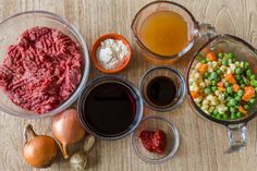 an assortment of food items including meat, vegetables and sauces on a wooden table