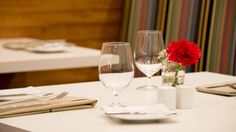 the table is set with two wine glasses, napkins and flowers in vases