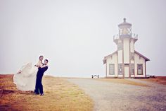 a bride and groom standing in front of a lighthouse