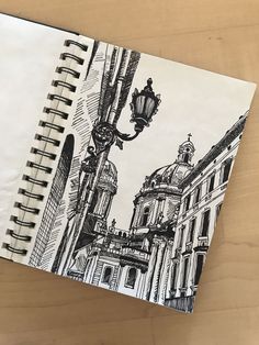 a notebook with a drawing of a street light and buildings in the background on a wooden table