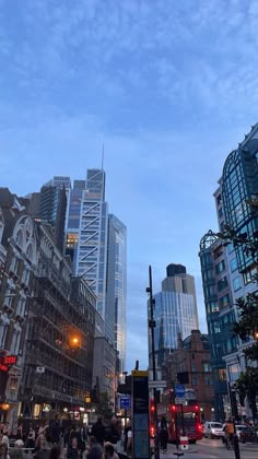 people are walking on the sidewalk in front of tall buildings at dusk, with street lights and traffic signals