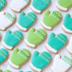 decorated cookies in the shape of mittens and gloves on a white tablecloth with green and blue frosting