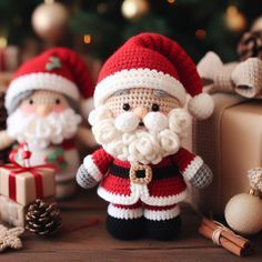 two crocheted santa clause figurines sitting next to presents on a table