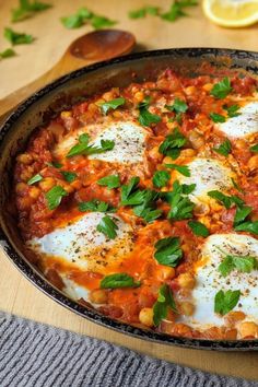 an iron skillet filled with eggs and tomato sauce on top of a wooden table