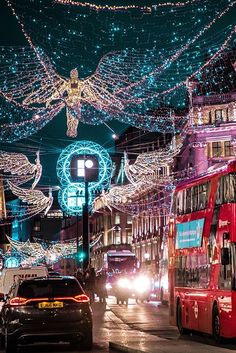 a red double decker bus driving down a street covered in christmas lights and garlands