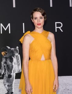 a woman in a yellow dress standing on a black and white background with an astronaut poster behind her